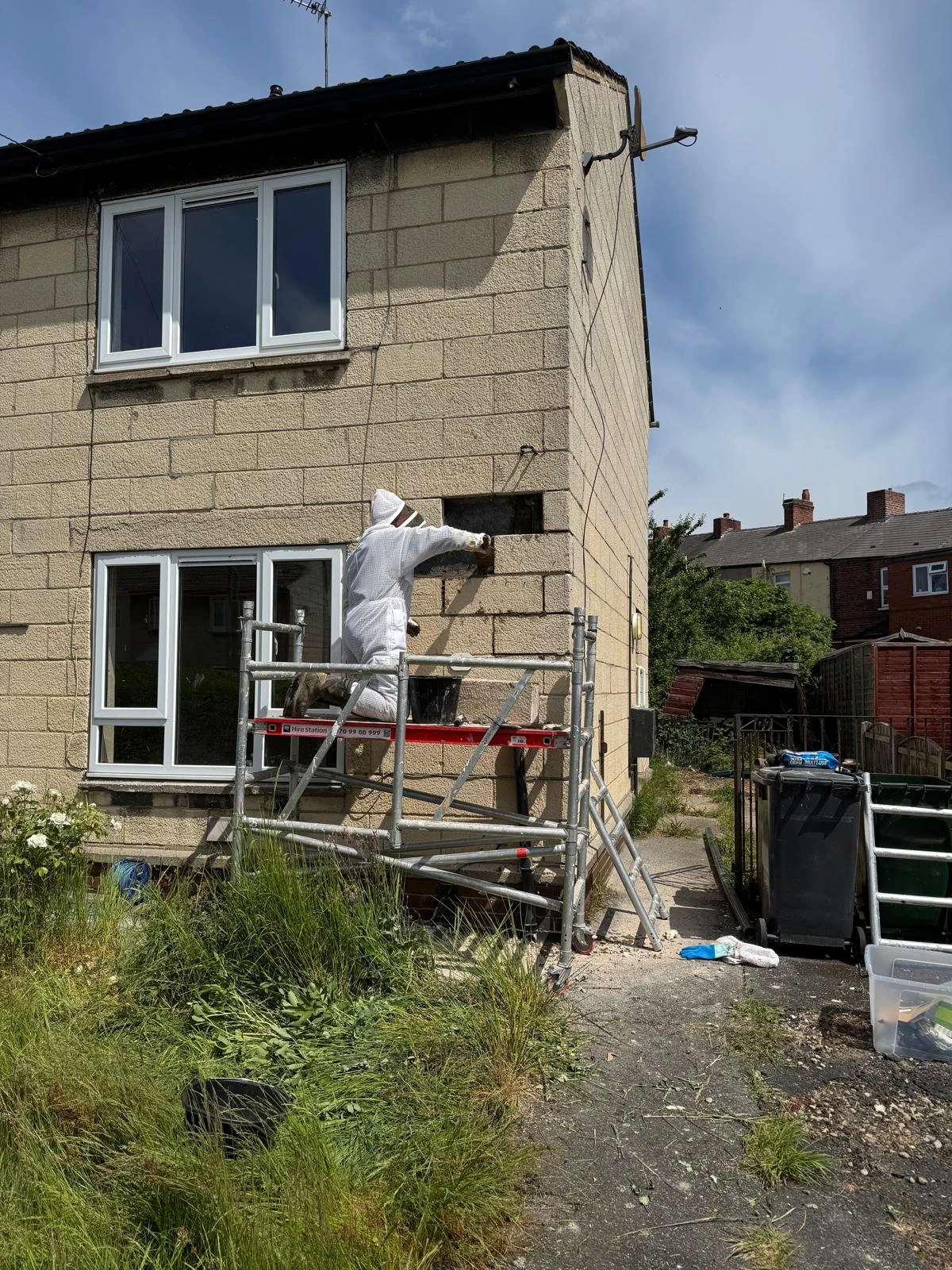 Apex technician in bee safety suit gaining access to a house cavity wall